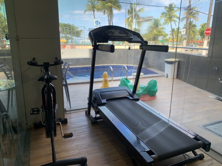 Esteira e bicicleta ergométrica em sala envidraçada, com a piscina ao fundo