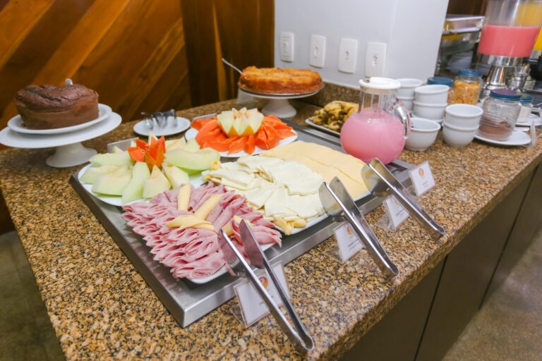 Bandeja com presunto, queijos e frutas fatiadas, com jarra de suco ao lado