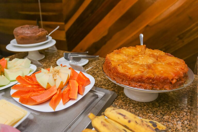 Bolo de abacaxi e bolo de chocolate ao lado de melão e mamão fatiados