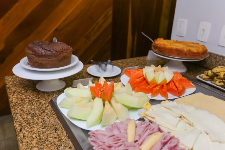 Bolo de chocolate, bolo de abacaxi, mamão, melão e frios servidos na bancada