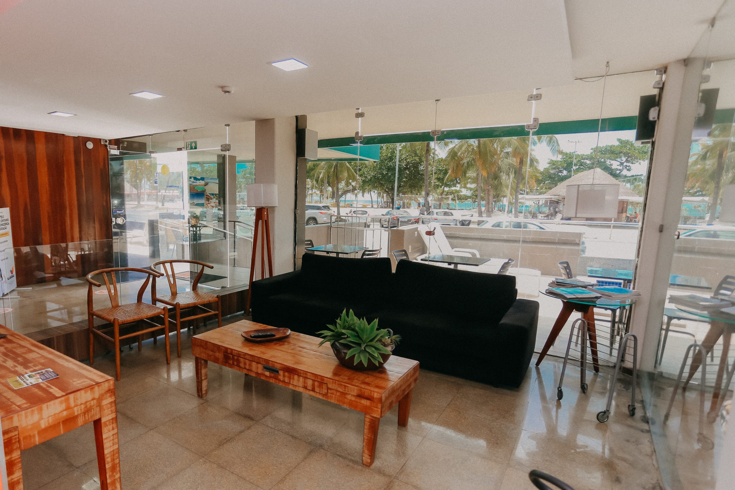 Lobby do hotel com sofás, mesas e janelas envidraçadas voltadas para a avenida da orla