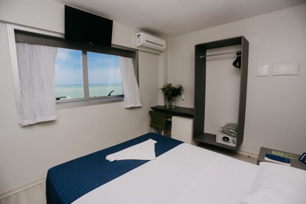 Apartamento Luxo com cama de casal, armário aberto e janela voltada para o mar