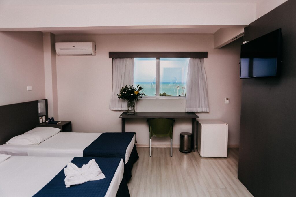 Apartamento Luxo com camas, escrivaninha, arranjo de flores e janela com vista para o mar