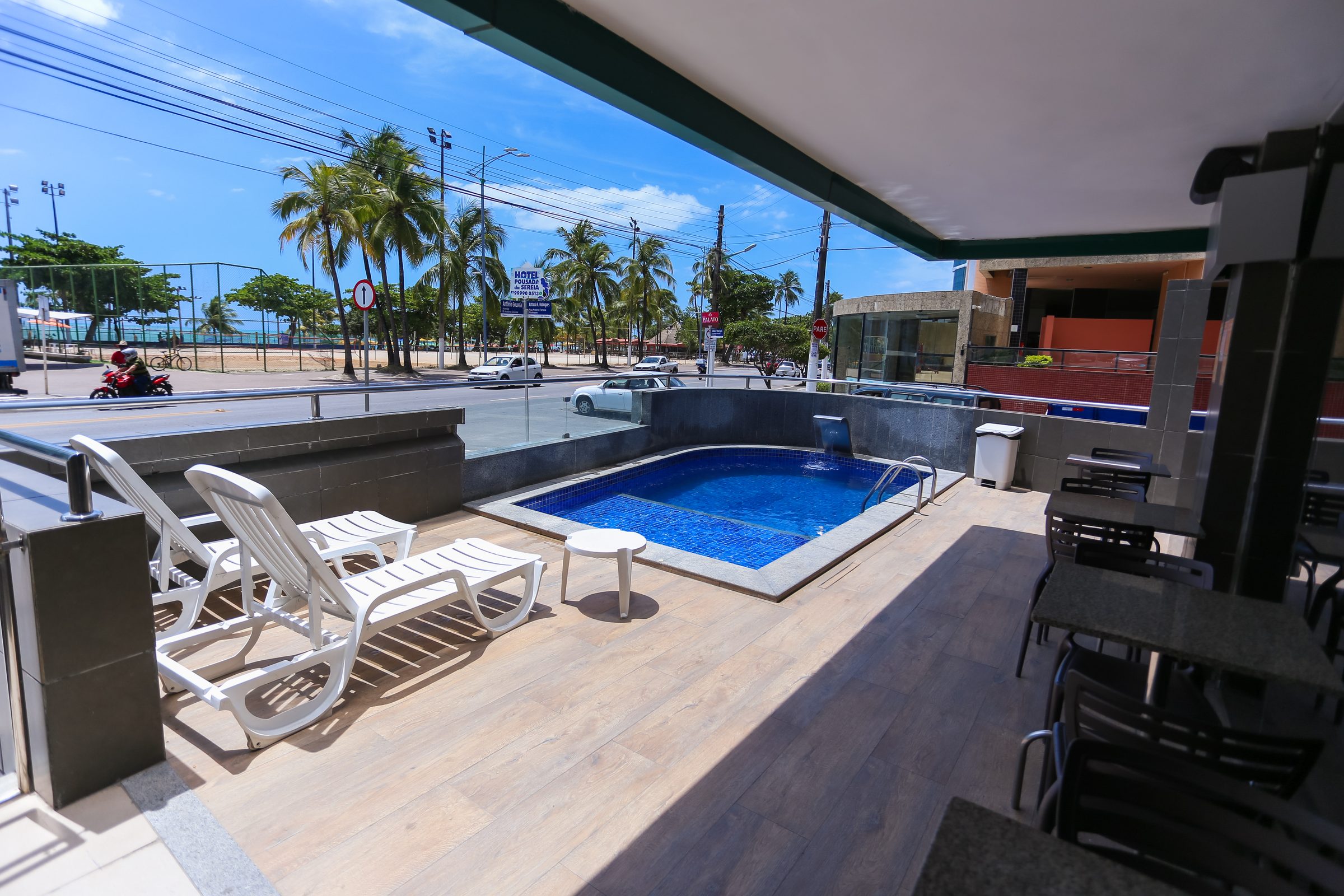 Piscina do hotel com espreguiçadeiras diante dos coqueiros da orla