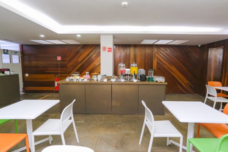 Salão do café da manhã com mesas e cadeiras montadas e o buffet ao centro